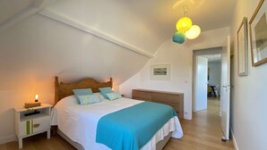 A bedroom with a bed, bedside tables, a nightstand, a ceiling light fixture, and a door leading to another room.