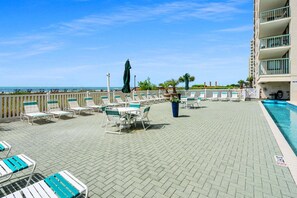 A rooftop pool area with lounge chairs and umbrellas, a pool, and a view of the ocean. - Deluxe oceanfront condos in the heart of North Myrtle Beach (North Myrtle Beach)