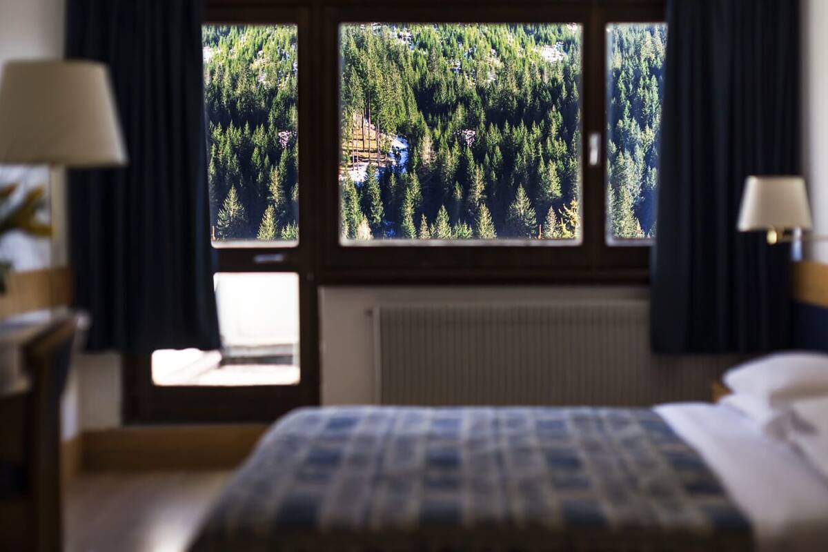 A hotel room with a bed, a desk, and a window offering a view of a forest.