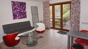A modern living room with a grey sofa, red and white chairs, a glass coffee table, and a large abstract painting on the wall.