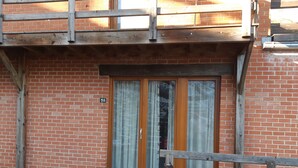 A brick building with a wooden balcony and a door with a curtain.