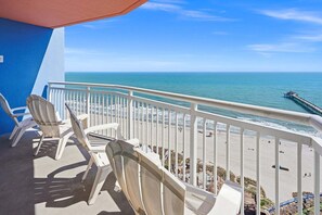 Ein Balkon mit weißen Stühlen und Blick auf Strand und Meer.