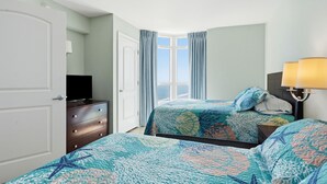 Una habitación de hotel con cama, tocador, televisor y ventana con cortinas.