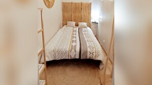 Habitació petita i acollidora amb un llit, un panell de fusta al capçal, una decoració circular a la paret i una làmpada penjant.