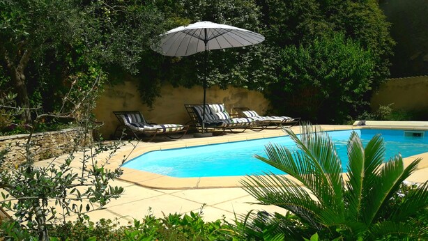 Una piscina amb gandules i una ombrel·la, envoltada de vegetació i un mur de pedra.