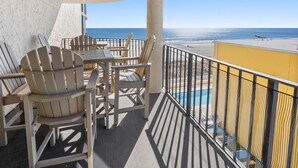 Ein Balkon mit Adirondack-Stühlen und einem Tisch, mit Blick auf einen Strand und ein Schwimmbad.