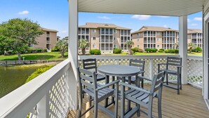 A covered outdoor area with a table and chairs, overlooking a body of water and a row of apartment buildings. - Condo in quiet resort w/amazing pool & Jacuzzi, great privte deck - 1 block from the beach (North Myrtle Beach)
