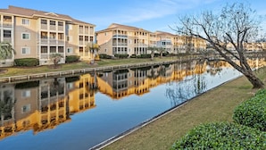A row of multi-story buildings with balconies, a calm water body reflecting the structures, and a clear sky. - Condo in quiet resort w/amazing pool & Jacuzzi, great privte deck - 1 block from the beach (North Myrtle Beach)