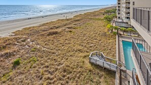 Um imóvel à beira-mar com piscina, praia e escadaria que leva a uma varanda.