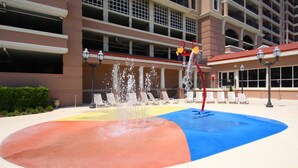 A water feature with multiple jets in a multi-colored area, surrounded by lounge chairs and a building with balconies. - Penthouse condo w/ stunning ocean views, pools, lazy river, and on-site cafe (Family-Friendly!) (North Myrtle Beach)