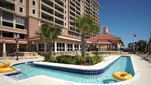 A hotel pool area with a large pool, lounge chairs, and palm trees. - Penthouse condo w/ stunning ocean views, pools, lazy river, and on-site cafe (Family-Friendly!) (North Myrtle Beach)
