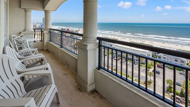 A balcony with white chairs, a view of the beach, and a clear sky. - Penthouse condo w/ stunning ocean views, pools, lazy river, and on-site cafe (Family-Friendly!) (North Myrtle Beach)