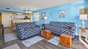 Ein Wohnzimmer mit zwei gestreiften Sofas, einem Holztisch und einer Küche im Hintergrund.