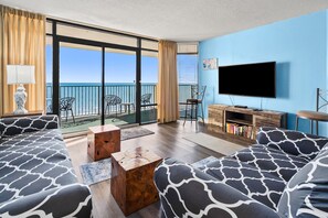 A living room with a large TV, wooden furniture, and a view of the sea. - Perfect blend of comfort and style for your next beach getaway (North Myrtle Beach)
