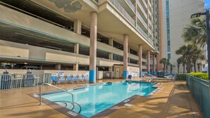Zona de piscina de hotel con un aparcamiento de varios niveles al fondo.