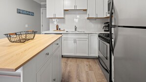 A modern kitchen with white cabinets, a wooden countertop, a stainless steel refrigerator, and a coffee maker. - Family & fishermen-friendly condos at quiet resort with pool and pier (North Myrtle Beach)