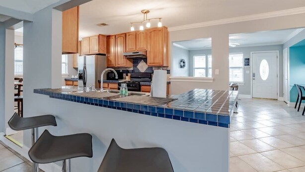 Uma cozinha moderna com armários de madeira, uma ilha central com banquetas e painel de azulejos.