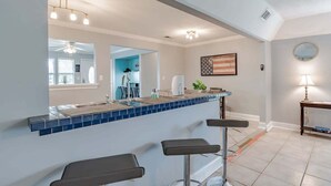 Uma cozinha com painel de azulejos azuis, um espaço de bar com banquetas e um ventilador de teto.