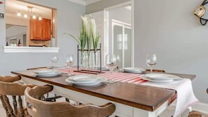 Uma sala de jantar com uma mesa de madeira comprida posta para seis pessoas, rodeada por cadeiras de madeira.