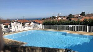 Une piscine entourée d’une clôture blanche, bordée de maisons aux toits rouges, et une grue visible au loin.