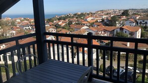 Un balcon offrant une vue sur une ville côtière, avec des maisons à étages et un ciel dégagé.