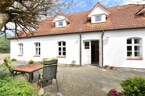 A white building with a red-tiled roof, a wooden table with chairs, and potted plants. - App.2 / 1-room (2 adults), attic - Ferienwohnungen Zum Breitling OVS 691 (Insel Poel)