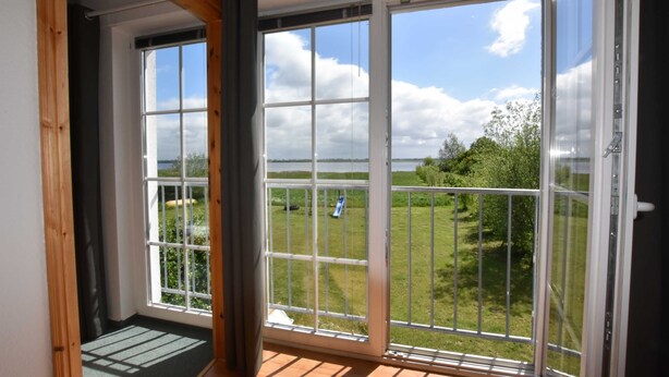 Une pièce dotée de grandes portes-fenêtres coulissantes qui donnent sur un balcon offrant une vue sur un espace verdoyant et des arbres.