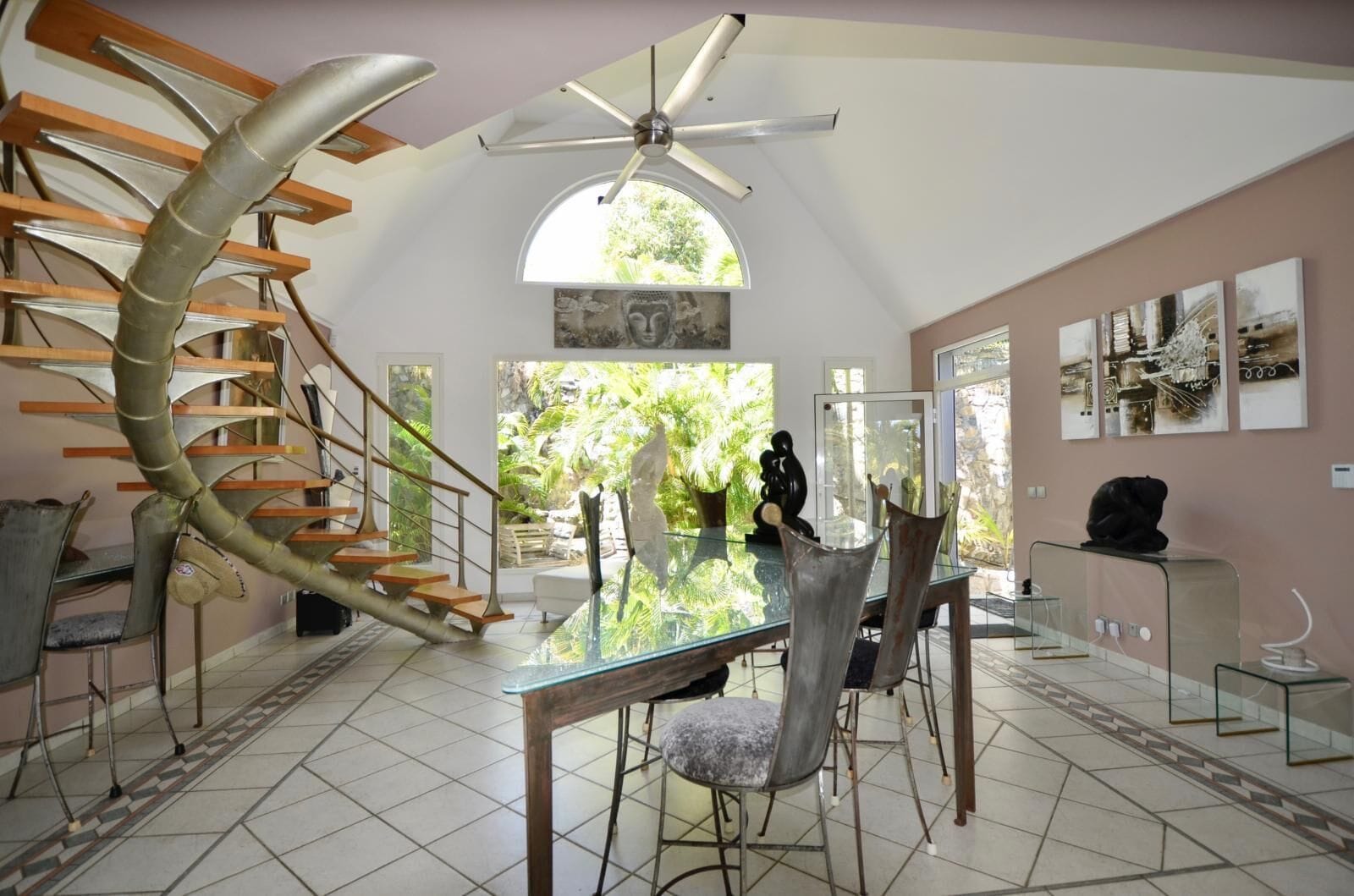 A modern interior with a spiral staircase, a dining area with glass tables, and a view of greenery outside.