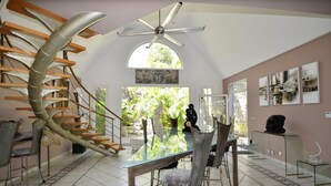 A modern interior with a spiral staircase, a dining area with glass tables, and a view of greenery outside. - Studio Boudha Zen   Residence Adam et Eve (Baie Orientale)