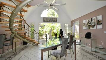 A modern interior with a spiral staircase, a dining area with glass tables, and a view of greenery outside.