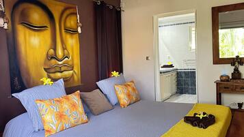 Une chambre avec un grand lit, un plaid jaune et un tableau représentant un Bouddha accroché au mur.