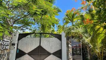A gated entrance with a geometric design, a stone wall, and a signboard with amenities and contact information.