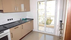 A kitchen with beige cabinets, a black countertop, and a glass door leading to a balcony. - Royal Palm 218, with panoramic sea view (Cannes)