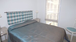 A bedroom with a bed, a nightstand, a chair, and a window with blinds. - Royal Palm 218, with panoramic sea view (Cannes)