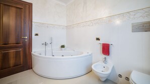 A bathroom with a large bathtub, a bidet, a toilet, and a wooden door.