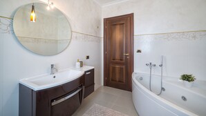 A modern bathroom with a round mirror, two sinks, a bathtub, and a wooden door.