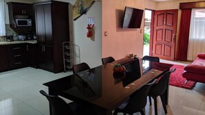 A modern kitchen with dark cabinets, a microwave, and a dining area with a glass table and chairs. - Hotel Suites Merlyn Airport (San Juan)