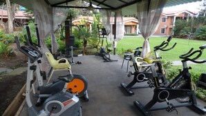 An outdoor gym with stationary bikes, treadmills, and elliptical machines under a covered area with a view of a residential neighborhood. - Hotel Suites Merlyn Airport (San Juan)