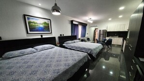 A hotel room with two beds, a kitchenette, and a painting on the wall. - Hotel Suites Merlyn Airport (San Juan)