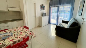 Un espace de vie compact comprenant un coin cuisine, un espace repas avec une table et des chaises, un canapé et une grande fenêtre avec des rideaux.