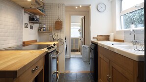 A modern kitchen with wooden cabinets, a stainless steel range hood, and a window with a view of greenery. - Crab Cottage (Whitstable)