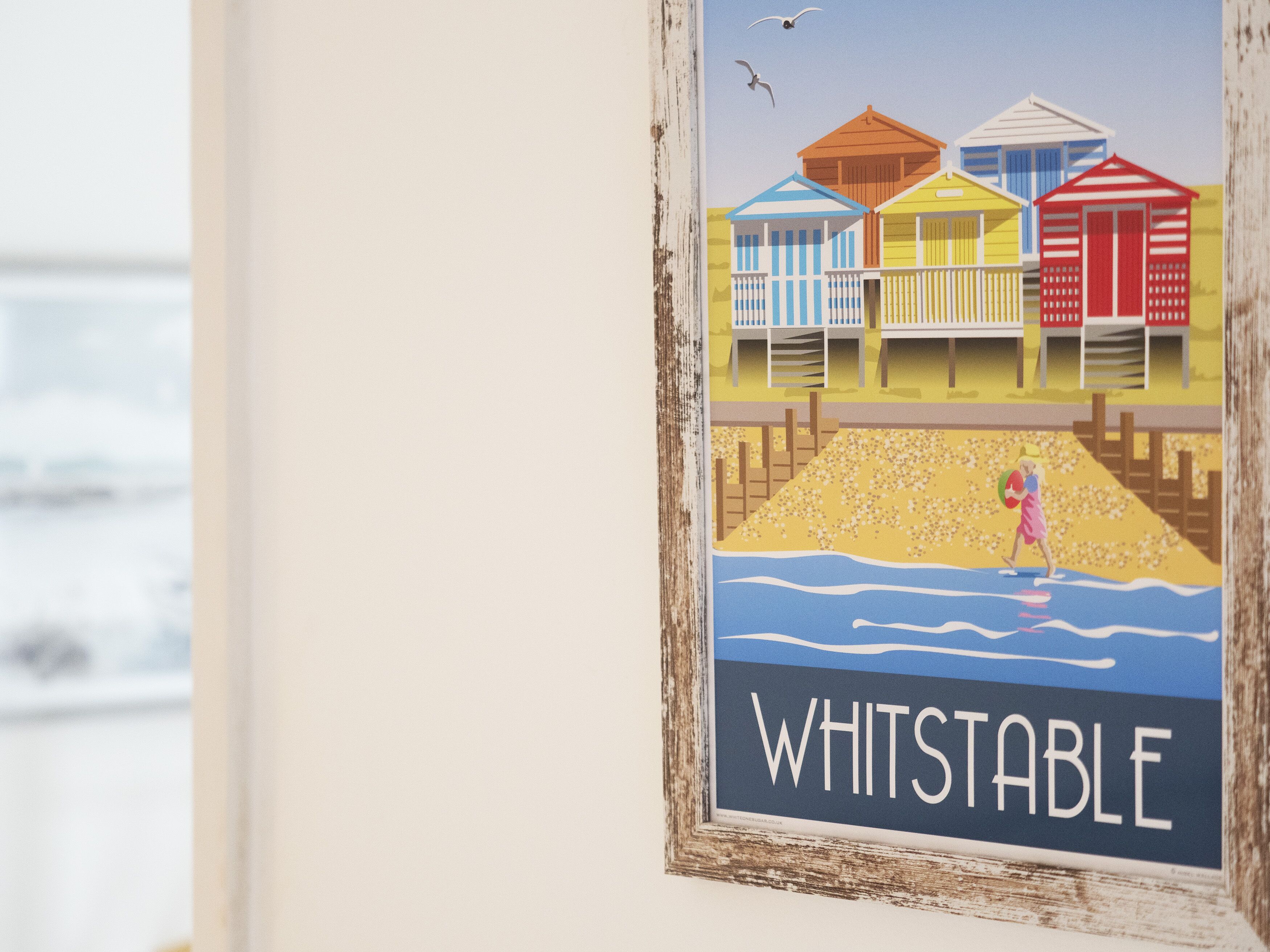 A framed artwork depicting beach huts and a person on a beach, with the text "WHITSTABLE" at the bottom.