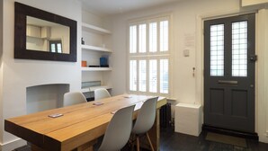 A modern dining area with a wooden table and white chairs, a built-in shelf unit, and a dark door with a window. - Crab Cottage (Whitstable)