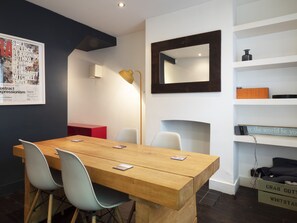 Una sala de conferencias moderna con una mesa de madera, sillas blancas, un armario rojo, una lámpara de pie, un espejo y estanterías con diversos objetos.