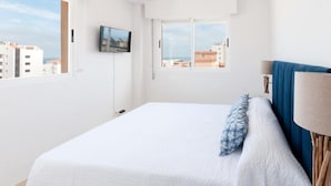 Ein Schlafzimmer mit einem Bett, einem an der Wand montierten Fernseher und einem Fenster mit Blick auf die Stadt.