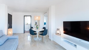 Ein modernes Wohnzimmer mit einer Couch, einem Esstisch mit Stühlen, einem Fernseher und einer Lampe.