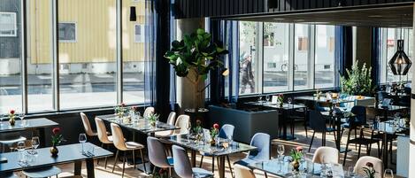 Ein modernes Restaurant mit großen Fenstern, Holzböden und einer Mischung aus Tischen und Sitzbänken.