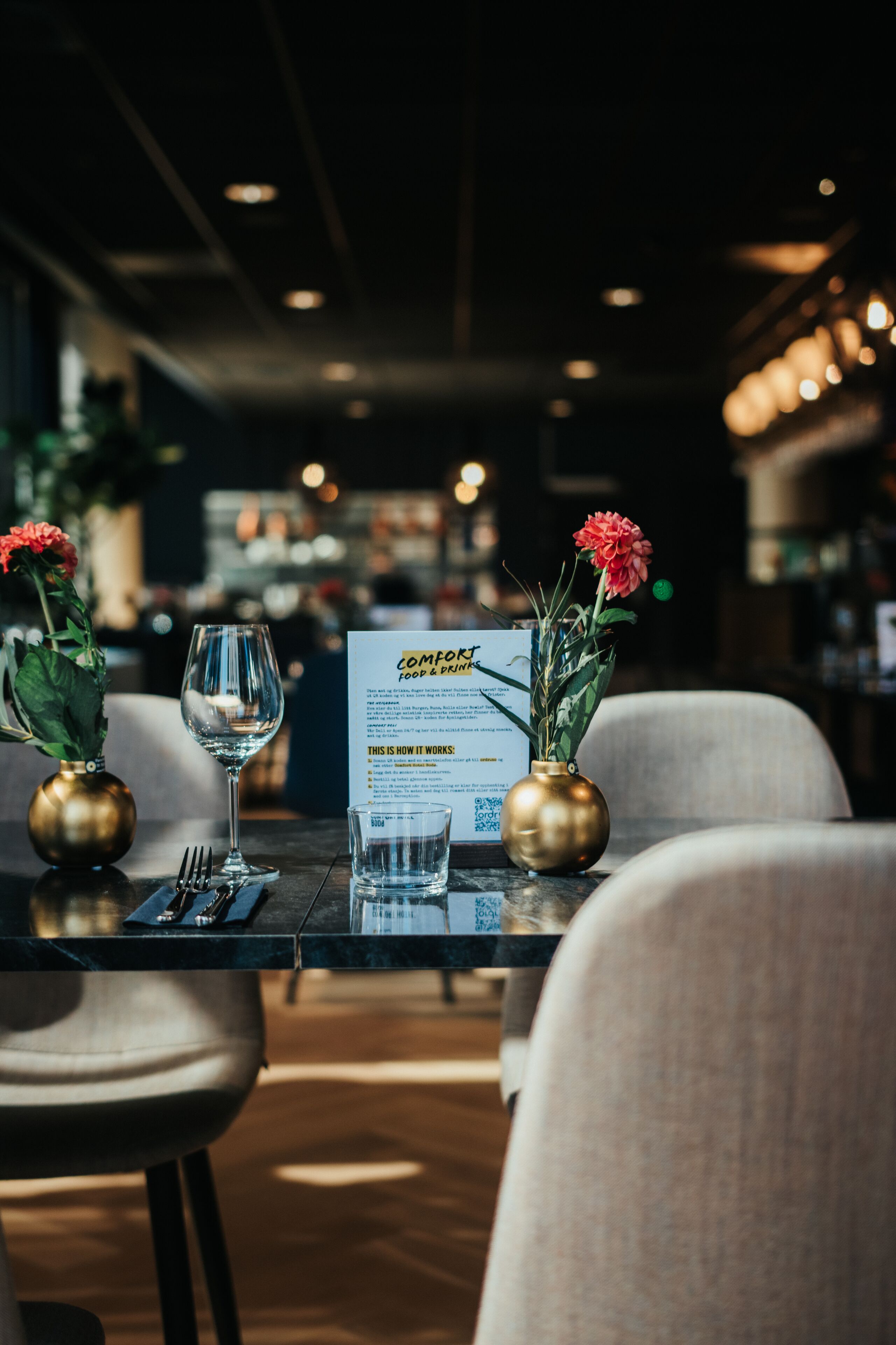 A dining table with a menu, two vases with flowers, a wine glass, and cutlery.