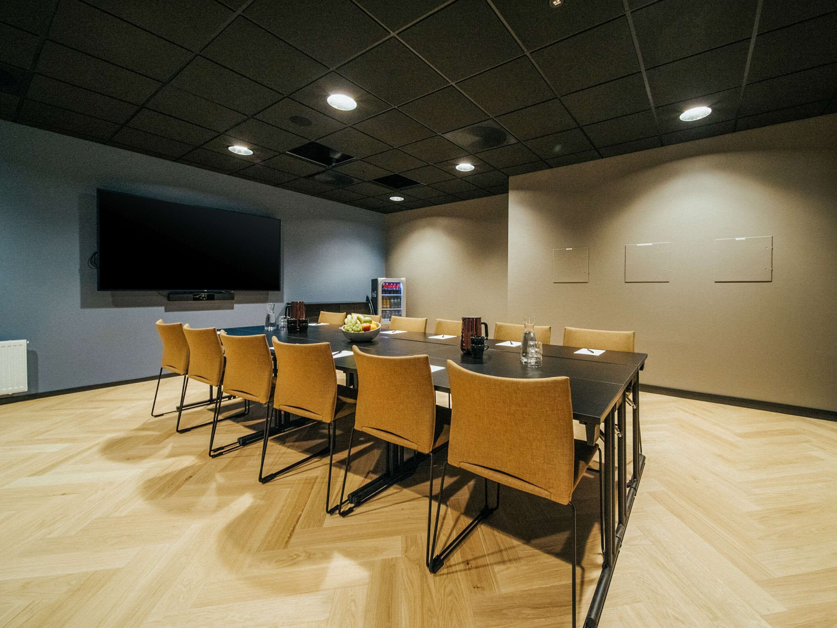 Una sala conferenze con un ampio tavolo, sedie, un televisore a schermo piatto, un distributore di bevande e un proiettore.
