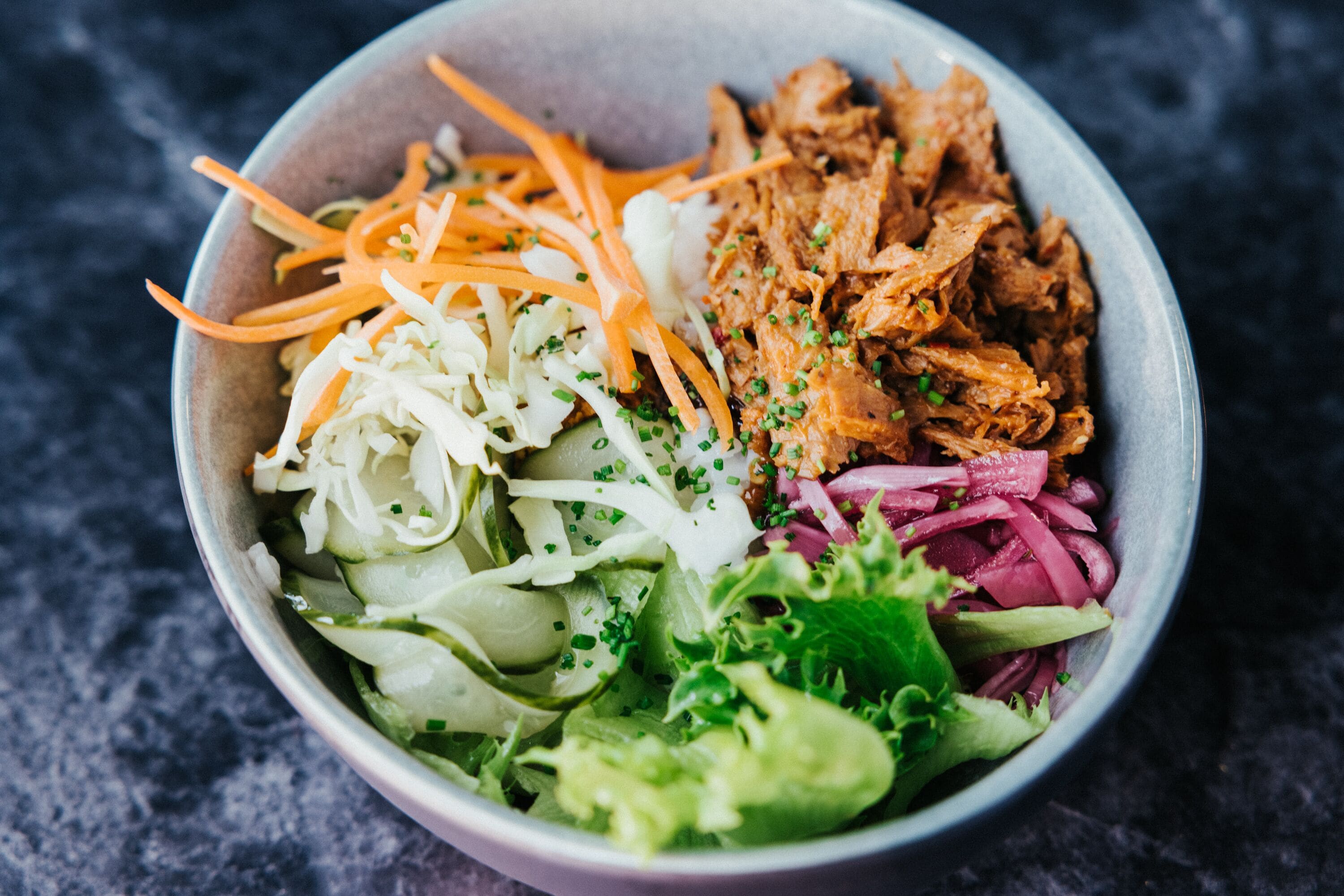 A bowl of salad with shredded carrots, shredded cabbage, shredded lettuce, and shredded red cabbage.